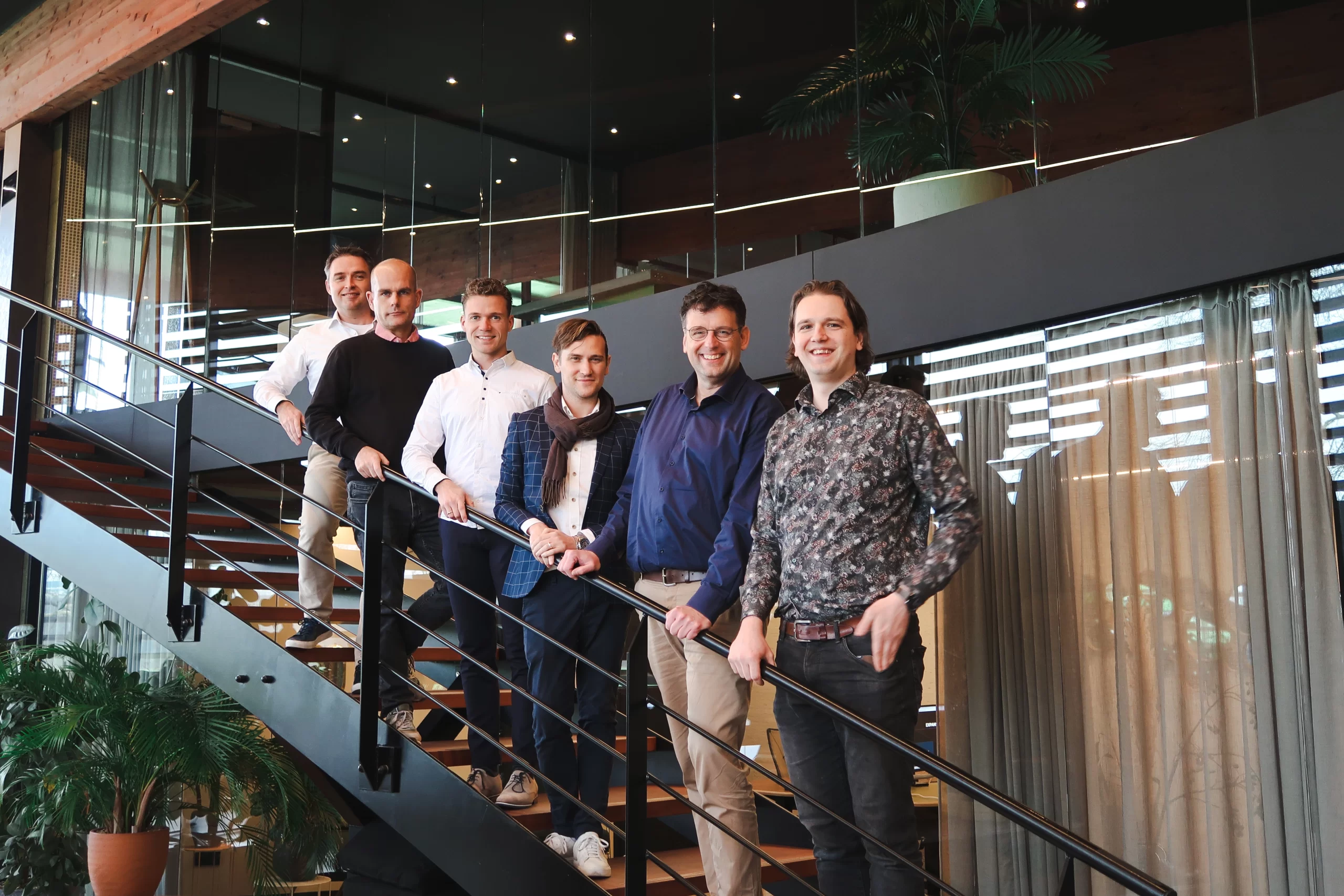 Green Fellows-team op een metalen trap in een kantoor met industriële uitstraling en veel glas.