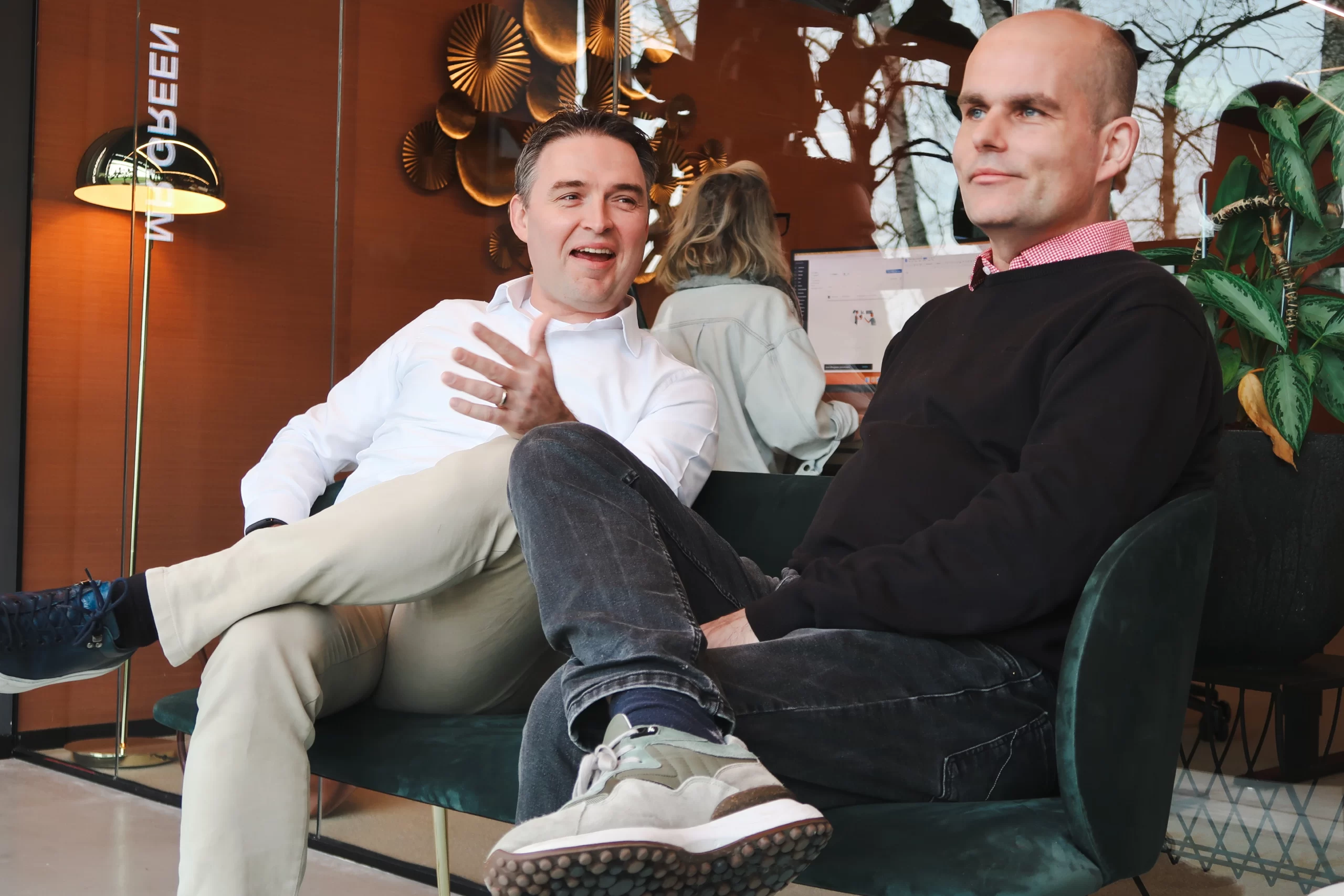 Henri en Arthur zitten ontspannen in een loungehoek met sfeervolle verlichting en groene planten.