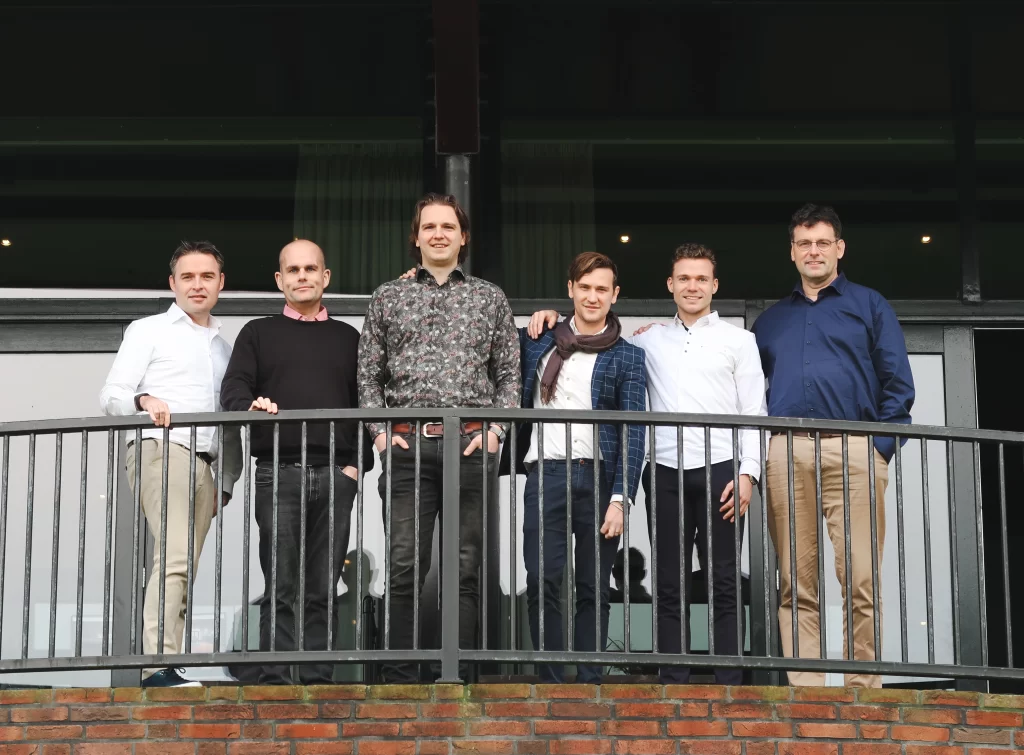 Het Green Fellows-team poseert buiten op een balkon, met een moderne kantoorgevel op de achtergrond.