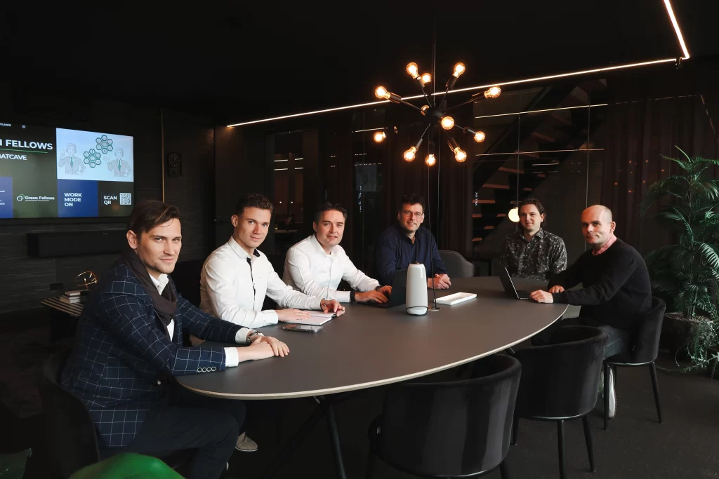 Green Fellows-teamleden in een vergaderruimte, zittend rond een houten tafel met een moderne inrichting.