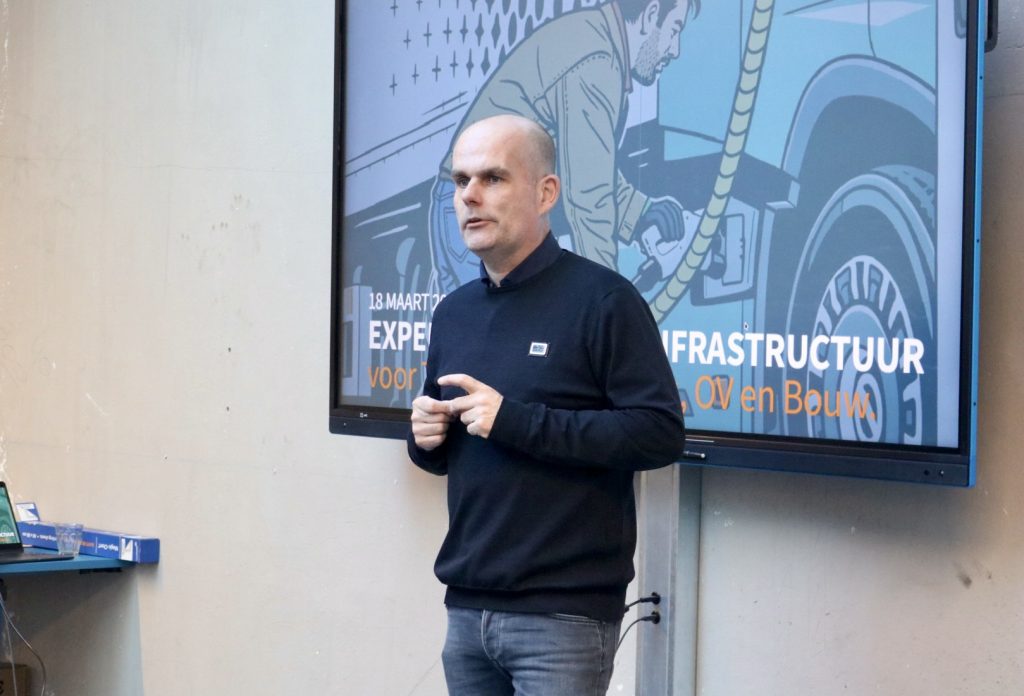 Henri Overbeek van Green Fellows geeft een presentatie over DC-laadinfrastructuur voor zware voertuigen, staand voor een scherm met visuele uitleg.